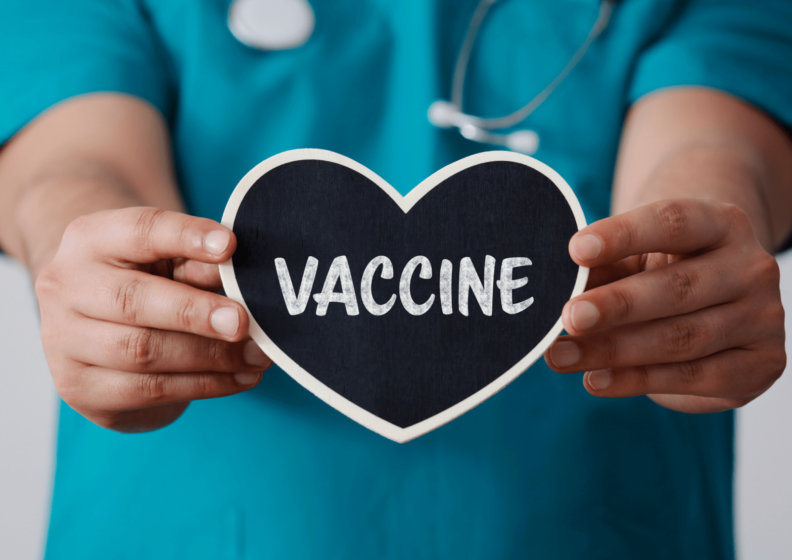 a doctor holding a heart-shaped sign which reads 'vaccine'